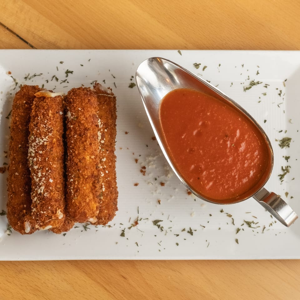 Crispy breaded mozzarella sticks garnished with herbs, served on a white platter with marinara sauce.