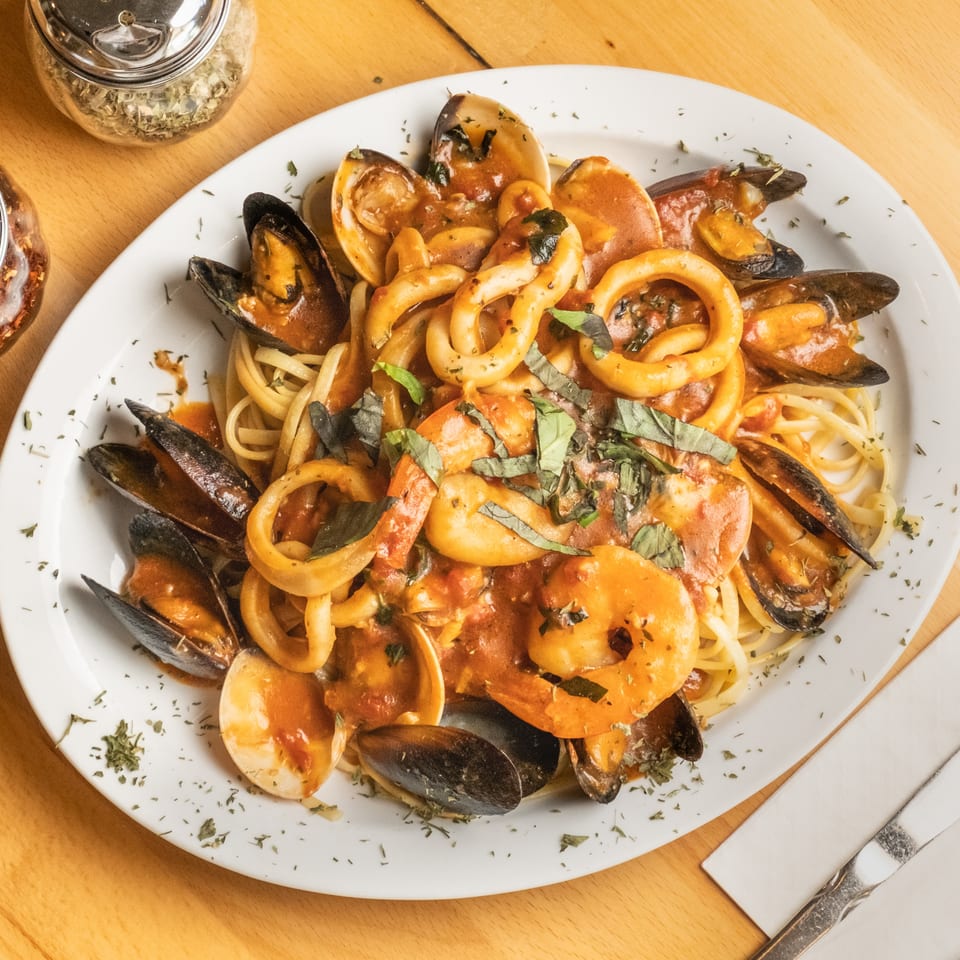 Seafood pasta with spaghetti, mussels, clams, shrimp, and calamari in tomato sauce, garnished with fresh basil.
