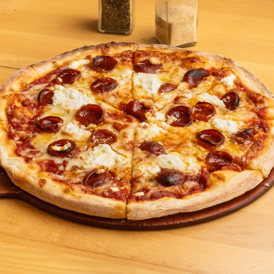 Whole pepperoni pizza topped with melted mozzarella and dollops of ricotta on a wooden serving board.