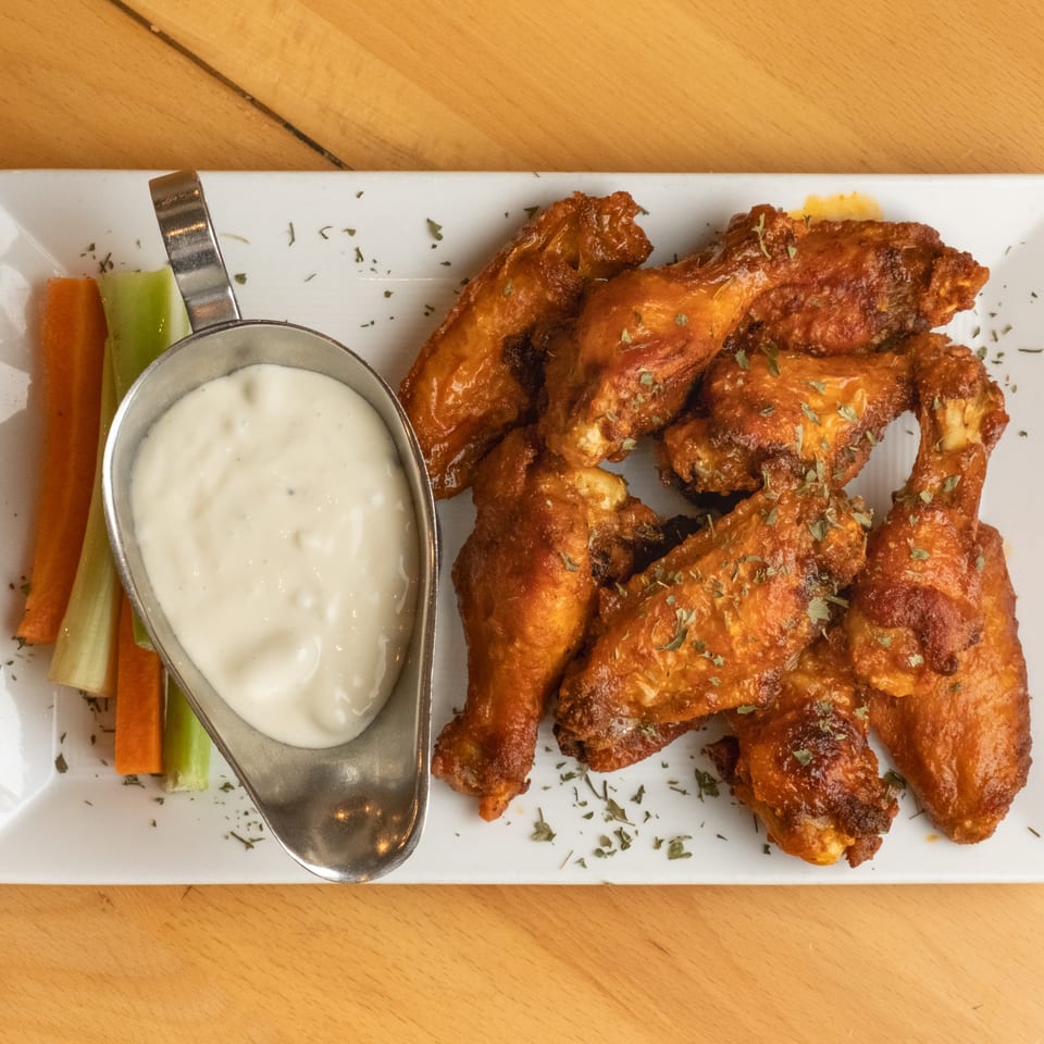 Plate of crispy buffalo chicken wings with ranch dressing, carrot and celery sticks on a wooden table.