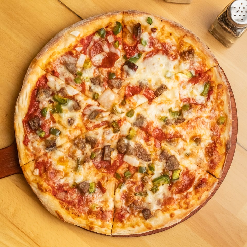 Large sliced pizza topped with melted cheese, pepperoni, mushrooms, onions, and green peppers on a wooden table.