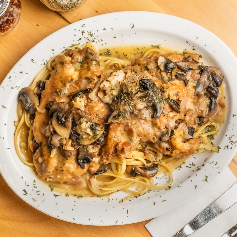 Creamy chicken and mushroom pasta topped with herbs, served on a white oval plate beside red pepper flakes.