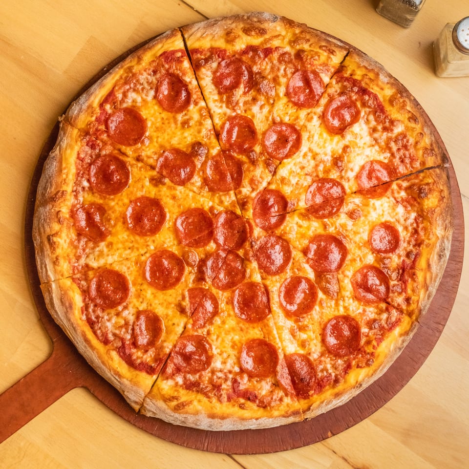 Large sliced pepperoni pizza with melted cheese on a wooden serving board, accompanied by salt and pepper shakers.