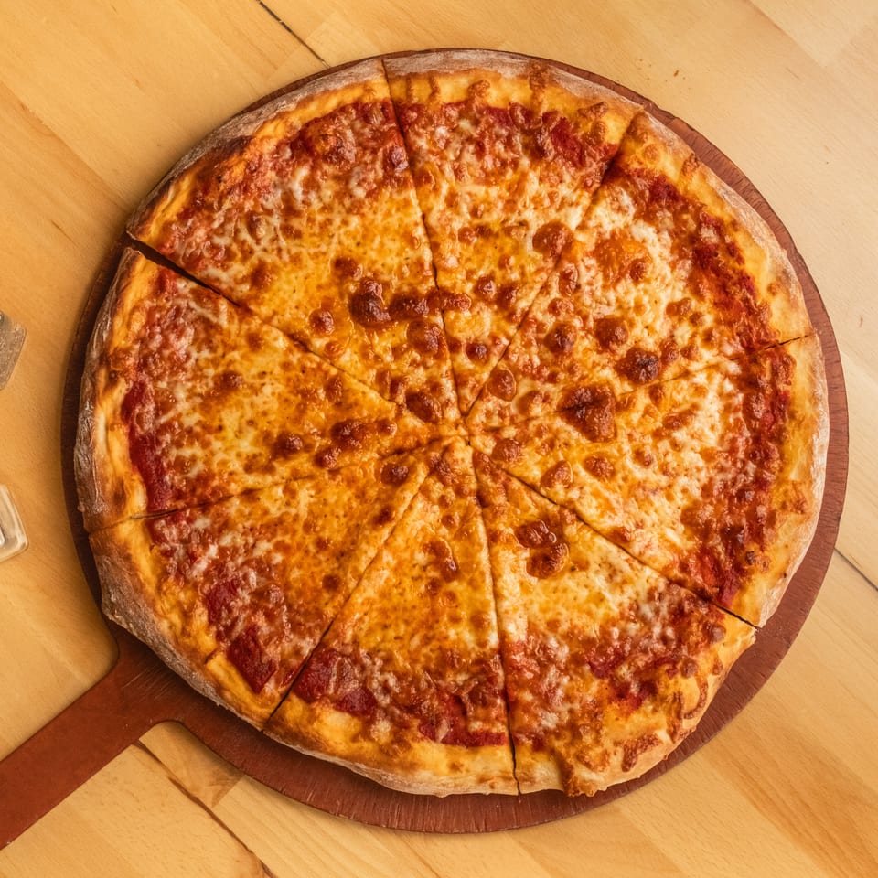 Large cheese pizza cut into slices on a wooden serving board, with salt and pepper shakers nearby.
