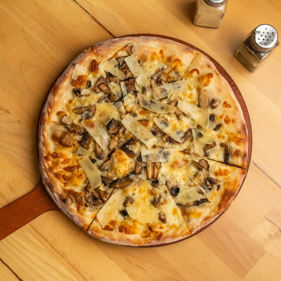 Cheesy mushroom pizza topped with shaved Parmesan on a wooden serving board, surrounded by salt and pepper shakers.