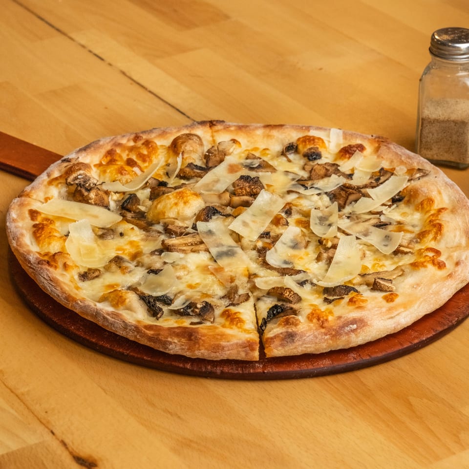 Mushroom pizza topped with melted cheese and shaved Parmesan sits on a wooden serving board beside salt and pepper shakers.